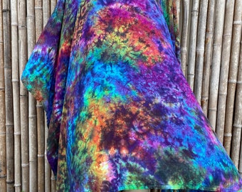 Może przedstawiać: Kolorowy ponczo w stylu tie-dye z dekoltem w kształcie litery V i asymetrycznym, falującym dołem. Ponczo wykonane jest z miękkiej, lekkiej tkaniny i charakteryzuje się żywą mieszanką kolorów: niebieskiego, fioletowego, zielonego, pomarańczowego i żółtego.