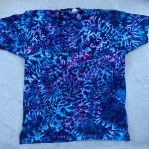 May include: A tie-dye t-shirt in shades of blue, purple, and white. The shirt has a swirling pattern and is made of a soft, comfortable fabric.
