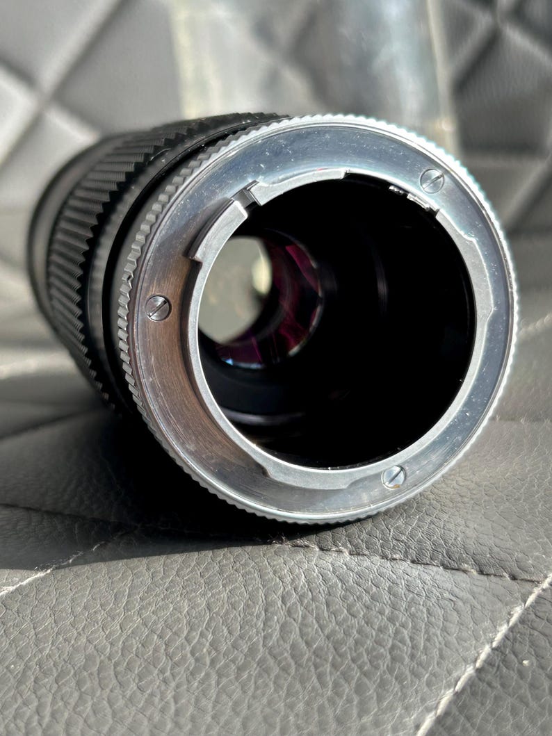 May include: Close-up of a black camera lens with a silver-colored mounting ring. The lens has a ridged focus ring and a clear aperture. The lens is designed for use with a camera.