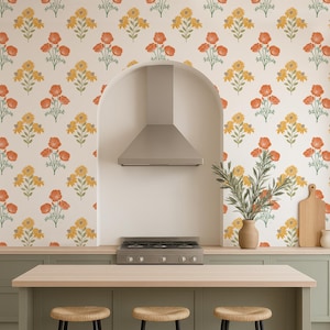 May include: A kitchen with a light green island and three black-legged stools with woven seats. The countertop is light wood. The backsplash features a floral pattern with orange and yellow flowers. A stainless steel range hood is above the stove.
