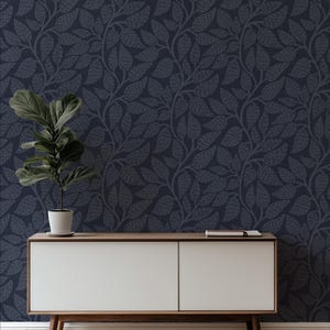 May include: Dark navy wallpaper with a repeating pattern of stylized leaves and vines. A white and wood-toned cabinet with a potted plant and a book sits in front of the wallpaper. The cabinet has two doors and angled legs.