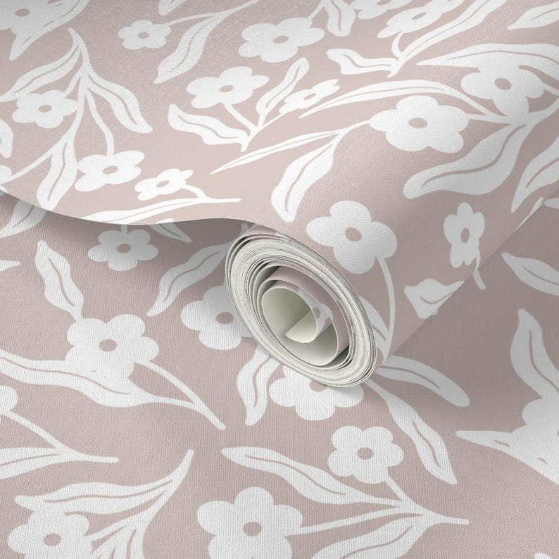 May include: A roll of wallpaper featuring a repeating pattern of white flowers and leaves on a muted pink background. The floral design is stylized and creates a soft, inviting aesthetic. The wallpaper is partially unrolled, revealing the pattern.