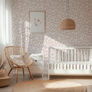 May include: A nursery interior with a white crib, a woven chair, and a round jute rug. The walls are covered in a floral wallpaper. A framed print hangs on the wall, and a woven pendant light hangs from the ceiling. The room is filled with natural light.