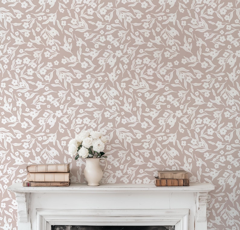 May include: A room with a floral wallpaper design in a neutral color palette. The wallpaper features a repeating pattern of white flowers and leaves on a light brown background. A white mantel holds a vase of white flowers and a stack of books.
