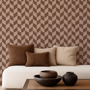 May include: A living room scene featuring a white sofa with four throw pillows in shades of brown and beige. A dark brown coffee table holds two ceramic bowls and a vase. The background is a brown and beige chevron pattern.