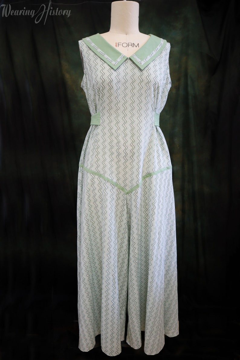 May include: A sleeveless dress with a green and white chevron pattern. The dress has a wide, green collar with a white trim and a green sash at the waist.