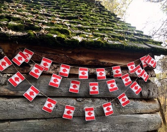 Pode incluir: Uma corda de bandeiras canadenses penduradas em um prédio de madeira com um telhado coberto de musgo. As bandeiras são vermelhas e brancas com um design de folha de bordo.
