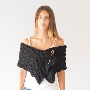 May include: A black knitted shawl with a cable knit pattern and a wooden toggle closure.