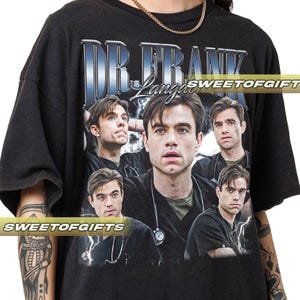 Puede incluir: Camiseta negra con un gráfico de un hombre y el texto "DR. FRANK" en azul y plata. El diseño incluye múltiples imágenes del hombre y un rayo. La camiseta tiene cuello redondo.