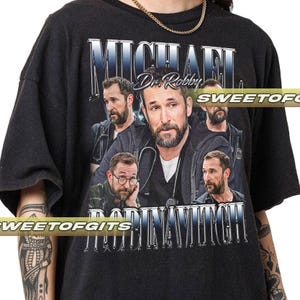 May include: Black t-shirt with a collage of images of Michael Robin Mitch, and the text "MICHAEL ROBIN MITCH" in a stylized font. The shirt also includes the text "Dr. Robby" in a script font.