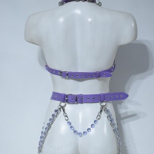 May include: A lavender purple harness set featuring a choker, a chest strap, and a waist belt with silver-toned metal buckles and eyelets. The waist belt is adorned with dangling silver chains and light purple faceted crystal beads.