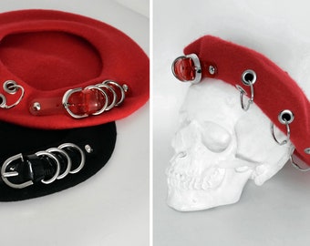 May include: Two berets, one red and one black, with silver metal rings and a red plastic band. The red beret is on a white skull.