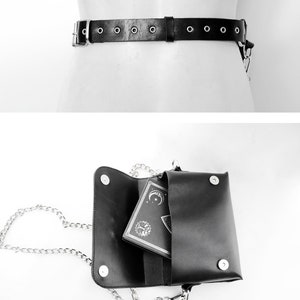 May include: A black leather belt with silver metal accents and a matching black leather bag with a silver chain strap. The bag is open and a small black book with a silver design is inside.