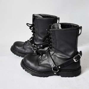 Puede incluir: Botas de cuero negro con hebillas y cordones. Las botas tienen una suela gruesa y un aspecto robusto.