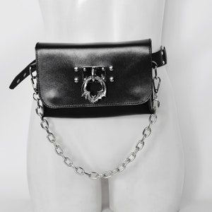 May include: Black leather fanny pack with a silver chain and a bat-shaped buckle. The bag has a flap with a silver ring.