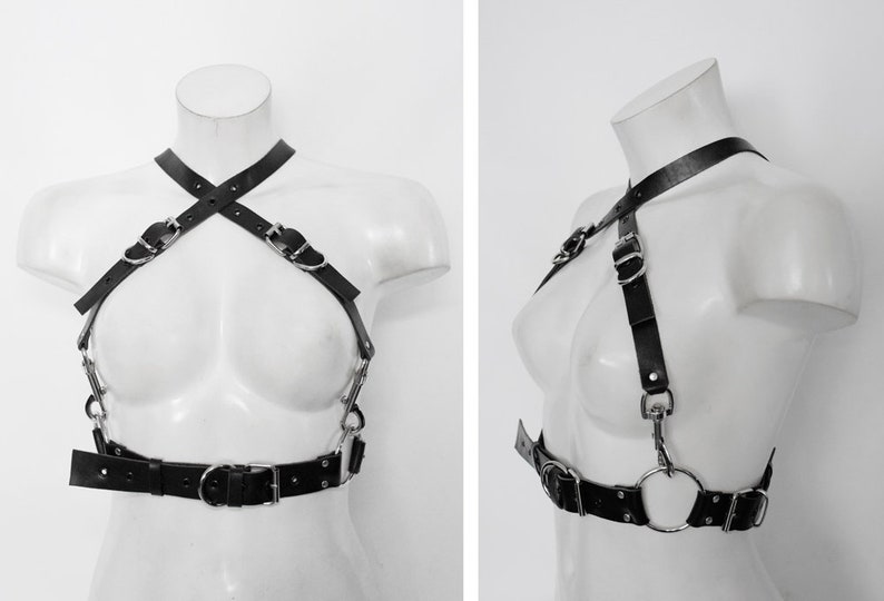 May include: Black leather harness with silver buckles and rings. The harness has a criss-cross design in the front and a belt with a large silver ring in the center.