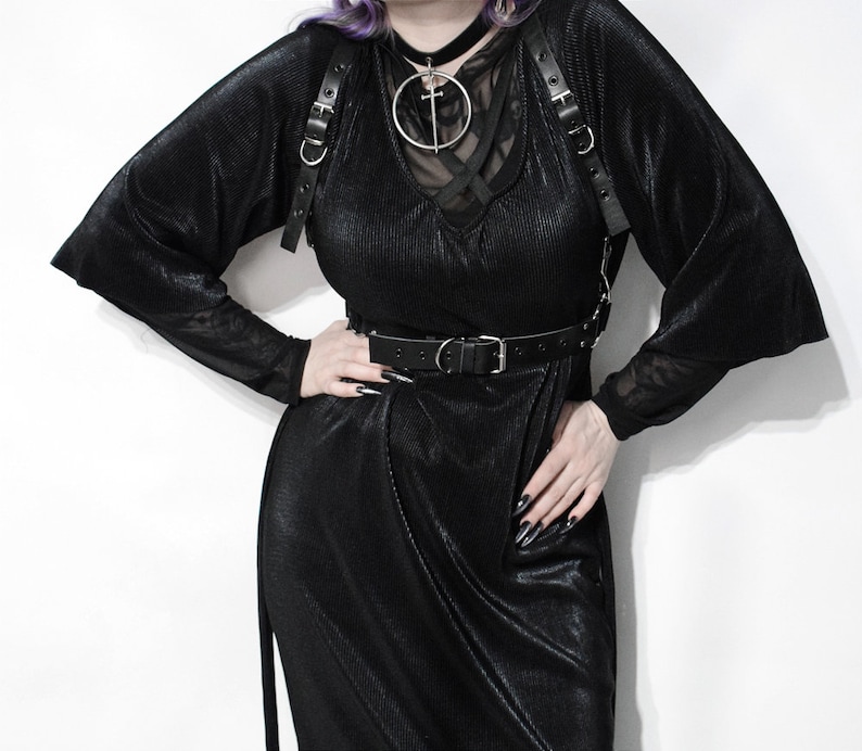 May include: A black velvet dress with a black leather harness and belt. The dress has a v-neck and long sleeves. The harness has a silver circle with a cross in the center.