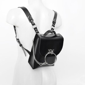 Puede incluir: Una mochila de cuero negro con un detalle de anillo plateado y una correa de cadena plateada.
