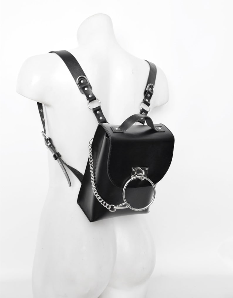 Puede incluir: Una mochila de cuero negro con un detalle de anillo plateado y una correa de cadena plateada.