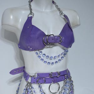 May include: A purple leather-like halter top and matching belt set featuring silver-tone metal chains, O-rings, and buckles. The garment is adorned with multiple strands of dangling light purple faceted crystal beads and silver metal chains.