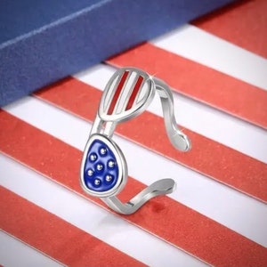 May include: A silver ring shaped like sunglasses with red and white stripes on the top and blue with white dots on the bottom.