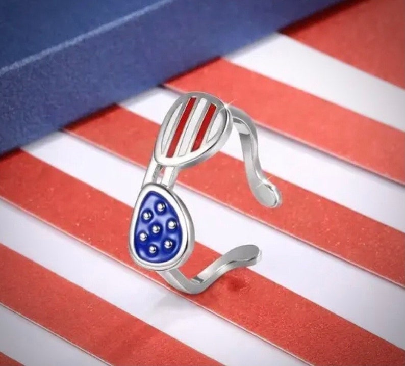 May include: A silver ring shaped like sunglasses with red and white stripes on the top and blue with white dots on the bottom.