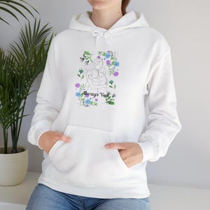Peut inclure: Un sweat-shirt à capuche blanc orné d'une illustration au trait représentant deux personnages s'enlaçant, entourés de fleurs bleues, violettes et vertes ainsi que de papillons, avec le texte noir Always You imprimé en dessous.
