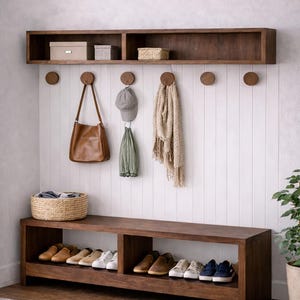 May include: A wooden hallway bench with a shelf above, displaying shoes, a woven basket, and hanging items such as a bag, hat, and scarf. The wall is white with vertical panelling.