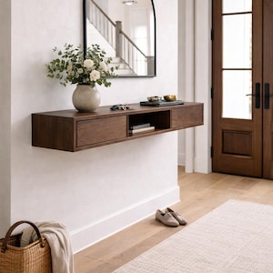 May include: A modern entryway with a dark wood floating console table, a black arched mirror, and a vase of flowers. A woven basket, a rug, and a pair of shoes complete the decor. The door is made of dark wood.