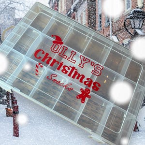May include: A clear plastic storage box with multiple compartments. The box is labelled "Olly's Christmas Snacks" in red letters with a candy cane and gingerbread man graphic.