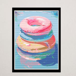 Può includere: Una stampa artistica incorniciata con una pila di colorati galleggianti gonfiabili per piscina. Il galleggiante superiore è rosa, seguito da blu e giallo. L'opera d'arte ha uno stile pixelato, digitale, con uno sfondo d'acqua blu.