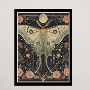Peut inclure: Une broderie au point de croix encadrée représentant un grand papillon de nuit aux ailes détaillées vertes et crème. Le motif comprend des roses roses, une pleine lune et un fond sombre avec des éléments décoratifs.