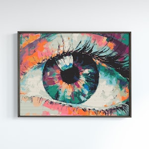 May include: A framed art print depicting a close-up of a human eye. The iris is a vibrant mix of colours including teal, orange, pink, and purple. The eyelashes are long and black. The artwork has a textured, pixelated appearance.