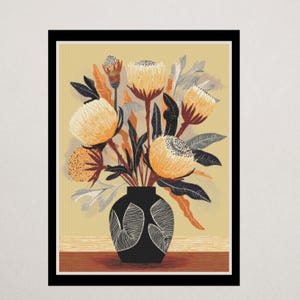 May include: A framed art print depicting a floral still life. The image shows orange and yellow flowers in a black vase with a decorative pattern. The leaves are dark green and grey. The background is a light yellow colour. The artwork is framed in black.
