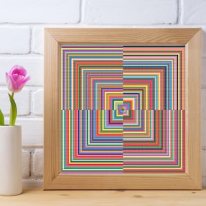 May include: A framed artwork with a vibrant, geometric pattern. The design consists of concentric squares in multiple colours, such as red, blue, green, and yellow. The frame is made of light wood. A pink tulip in a white vase is in the foreground.