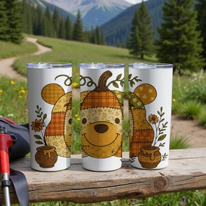 Op de afbeelding: Drie witte ge&iuml;soleerde bekers met een herfstthema-ontwerp. Elke beker heeft een cartoon beer karakter met een pompoen hoofd, patchwork en een honingpot. De achtergrond toont een berglandschap.