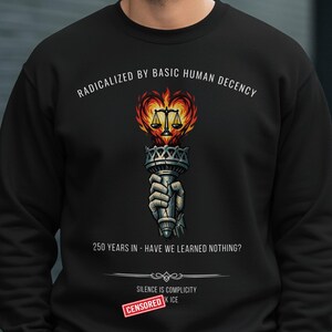 Peut inclure: Sweat-shirt noir avec un motif graphique d'une main tenant une torche, surmontée d'une flamme en forme de cœur et d'une balance. Le texte comprend "RADICALIZED BY BASIC HUMAN DECENCY" et "250 YEARS IN - HAVE WE LEARNED NOTHING?" avec un tampon "CENSORED".