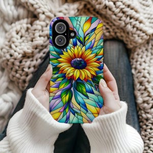 May include: A colorful phone case featuring a stained-glass design of a sunflower. The case has a vibrant mix of yellow, blue, green, and orange hues. The sunflower is the focal point, surrounded by geometric shapes. The case has two camera lenses.