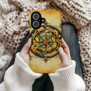 May include: A phone case featuring a vintage map design with a compass rose at the center. The case has a yellow background with intricate details in shades of brown, gold, and blue. The phone case is held by a person wearing a white sweater.
