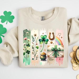 May include: A beige sweatshirt with a colorful graphic design featuring shamrocks, a horseshoe, a pot of gold, a rainbow, and a heart. The design is in a vertical stripe pattern.