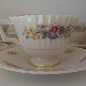 May include: A set of white teacups and saucers with a floral pattern in shades of pink, yellow, and blue. The cups have a fluted design and gold trim.