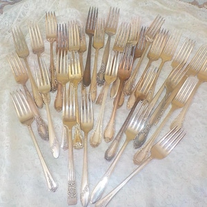 May include: A collection of vintage silver-plated forks featuring various ornate handle designs with intricate floral and scrollwork patterns. The assortment includes multiple dining forks with four tines, showcasing a mix of polished and tarnished metal finishes.
