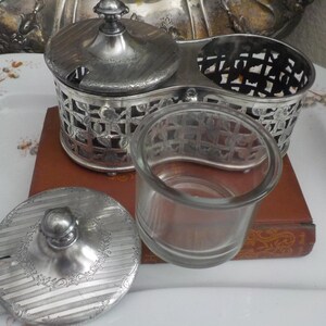 May include: Silver plated double condiment set with a glass jar and a lid. The set has a decorative design of leaves and flowers.