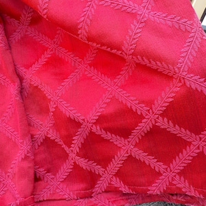 May include: A vibrant red fabric featuring a raised, textured grid pattern composed of delicate, repeating leaf-like motifs. The material displays a consistent crimson hue throughout, with the woven lattice design creating a subtle depth and dimension across the surface of the textile.