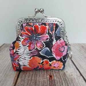 May include: A floral print coin purse with a silver metal clasp. The purse features a colorful pattern of red, pink, and orange flowers on a dark background. A small chain is attached to the clasp.