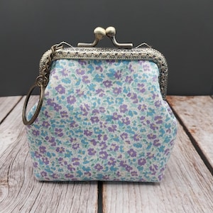 May include: A small, floral-patterned coin purse with a metal clasp and a ring for attaching keys. The purse features a light blue background with small purple and blue flowers. The metal clasp is silver-toned.