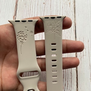 May include: Two beige silicone watch straps with floral designs. One strap features a dandelion and the other features a cluster of flowers.