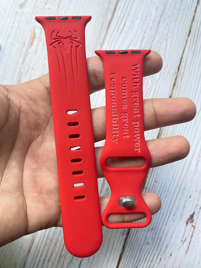 May include: Red silicone Apple Watch band with a Spiderman logo on one side and the text "With great power comes great responsibility" on the other side.