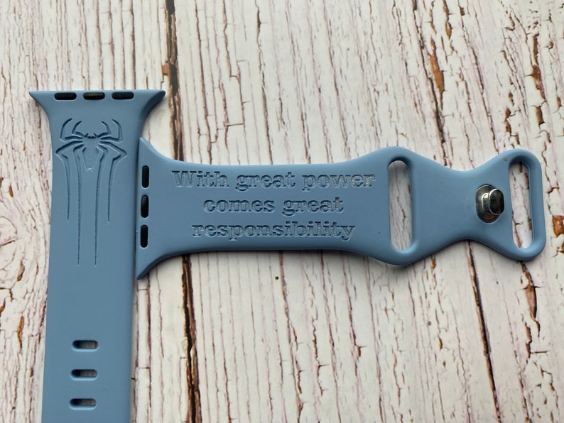 May include: A light blue silicone watch band with a Spiderman logo and the quote "With great power comes great responsibility" engraved on it.