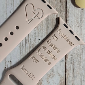 May include: A pink Apple Watch band with a cross and heart design and the text "Be joyful in your hope, Be patient in your tribulation, Be Constant in prayer, Romans 12:12".